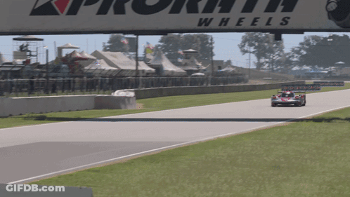 A Race Car Is Driving Down A Track Under A Sign That Says Wheels GIF