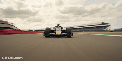 A Race Car Is Driving Down A Track With A Large Building In The Background GIF