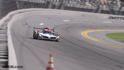 A Race Car Is Driving Down A Track With A Red And White Cone In Front Of It GIF