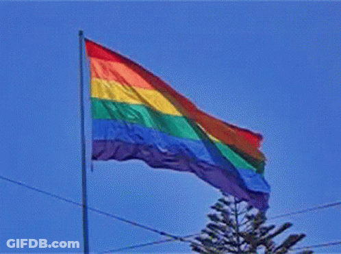 A Rainbow Flag Is Flying In A Blue Sky GIF