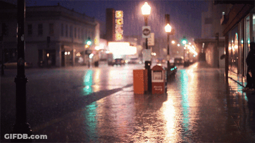 A Rainy City Street With A Sign That Says No Parking On It GIF