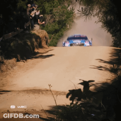 A Rally Car Is Driving Down A Dirt Road With A W2c Logo In The Corner GIF
