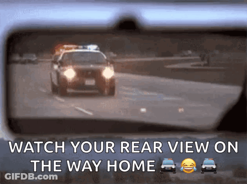 A Rear View Mirror Shows A Police Car Driving Down A Road GIF