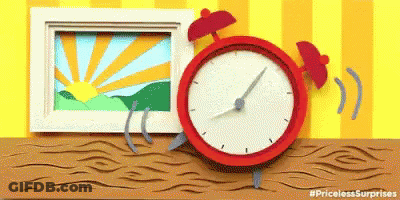 A Red Alarm Clock Is Sitting On A Wooden Table Next To A Picture Of A Sunrise GIF