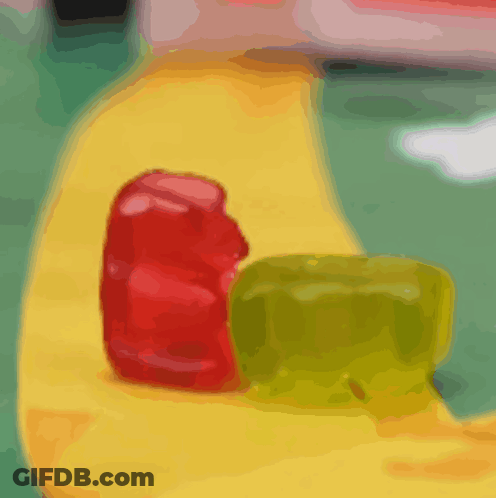 A Red And Green Gummy Bear Sit On A Yellow Surface GIF