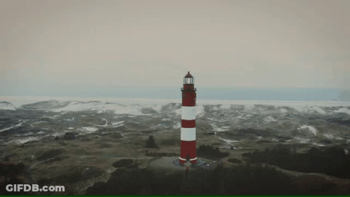 A Red And White Lighthouse Sits On Top Of A Hill GIF
