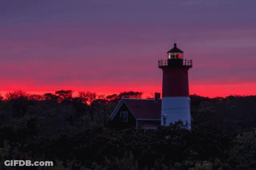 A Red And White Lighthouse Stands In Front Of A Sunset Sky GIF