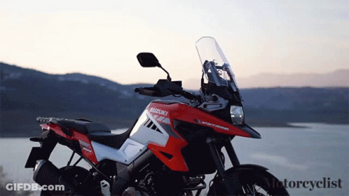 A Red And White Suzuki Motorcycle Is Parked Near A Lake GIF