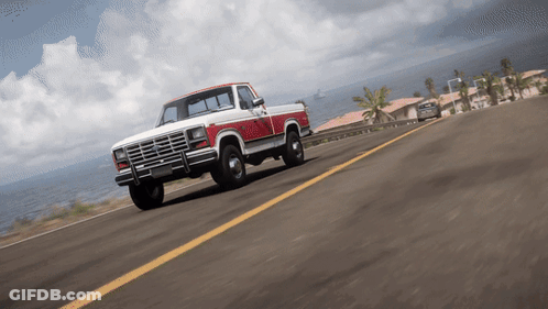 A Red And White Truck Is Driving Down A Road Near The Ocean GIF
