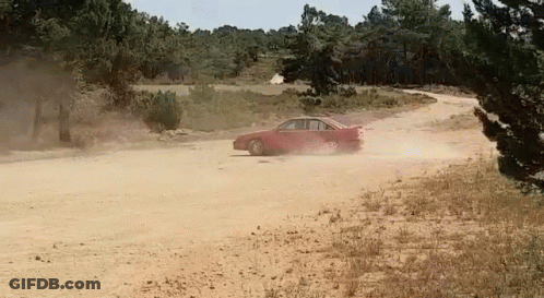 A Red Car Driving Down A Dirt Road With Trees In The Background GIF