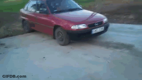 A Red Car Is Behind A Opel Logo On A Concrete Surface GIF