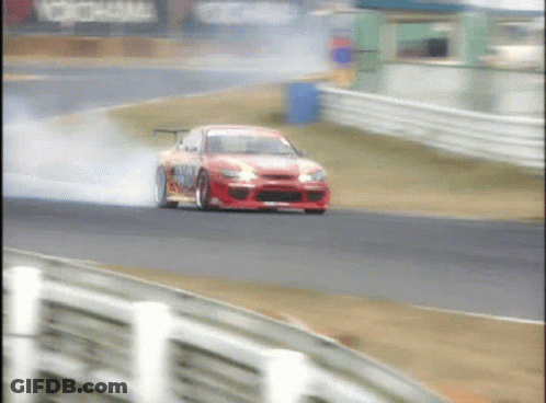 A Red Car Is Drifting On A Race Track With Smoke Coming Out Of The Tires GIF