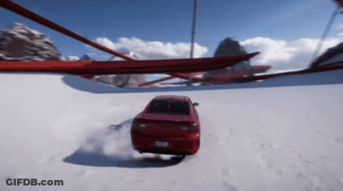 A Red Car Is Driving Down A Snowy Road With Mountains In The Background GIF