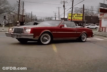 A Red Car Is Driving Down A Street In Front Of A Sign That Says We Buy Ugly Houses GIF