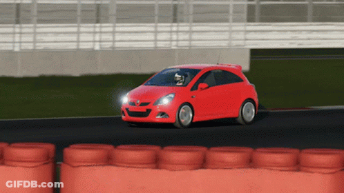 A Red Car Is Driving On A Track With A Row Of Orange Tires Behind It GIF
