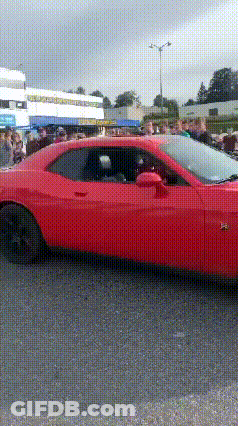 A Red Car Is Parked In A Parking Lot With A Crowd Of People Watching . GIF
