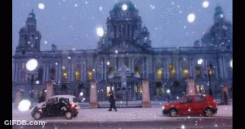 A Red Car Is Parked In Front Of A Building In The Snow GIF