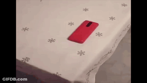 A Red Cell Phone Is Sitting On A White Surface Next To Snowflakes . GIF