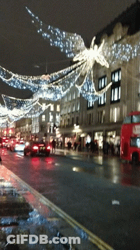 A Red Double Decker Bus Is Driving Down A Busy Street GIF