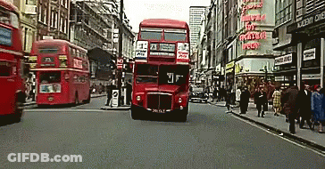 A Red Double Decker Bus Is Driving Down A Street GIF