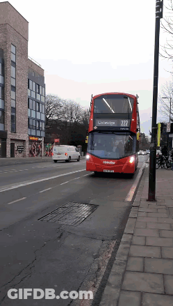 A Red Double Decker Bus With The Number 222 On The Front Is Driving Down A Street GIF