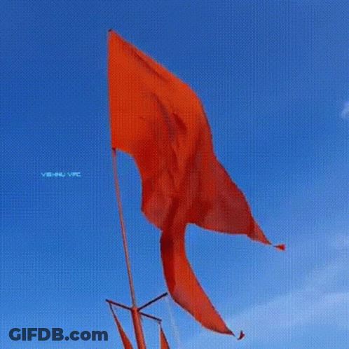 A Red Flag Is Flying In The Wind In Front Of A Blue Sky . GIF