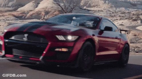A Red Ford Mustang Is Driving Down A Road GIF