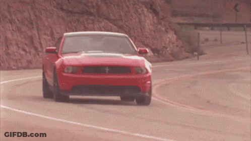 A Red Ford Mustang Is Driving Down A Road GIF