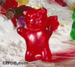 A Red Gummy Bear Is Sitting On A Table With Other Gummy Bears GIF