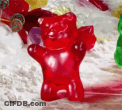 A Red Gummy Bear Standing In Front Of A Pile Of Candy GIF