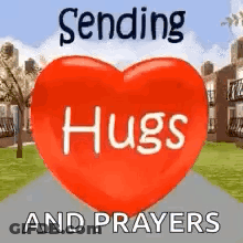 A Red Heart With The Words `` Sending Hugs And Prayers '' Written On It Is Sitting On A Sidewalk . GIF