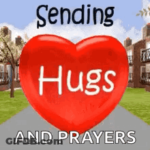 A Red Heart With The Words `` Sending Hugs And Prayers '' Written On It Is Sitting On A Sidewalk . GIF