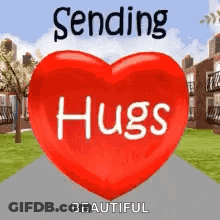 A Red Heart With The Words `` Sending Hugs '' Written On It Is Sitting On A Sidewalk . GIF