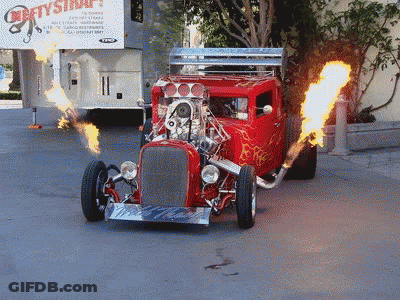 A Red Hot Rod With Flames Coming Out Of It Is Driving Down A Street GIF