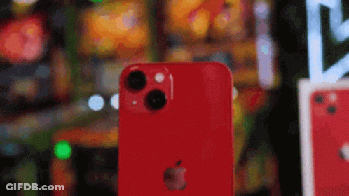 A Red Iphone Is Sitting On A Table In Front Of A Blurred Background . GIF