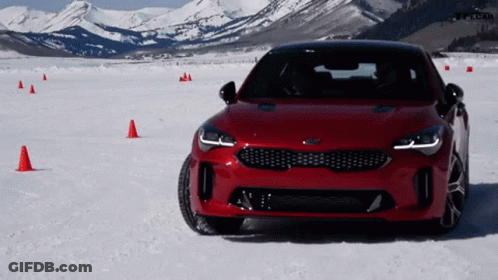 A Red Kia Car Is Parked In The Snow With Mountains In The Background GIF