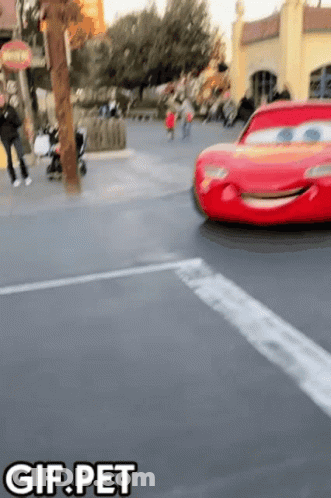 A Red Lightning Mcqueen Car Is Driving Down A Street With The Words Gif.pet Below It GIF
