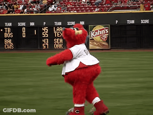 A Red Mascot On A Baseball Field With A Kahn 'S Ad In The Background GIF