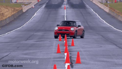 A Red Mini Cooper Is Driving On A Wet Road Surrounded By Red Cones GIF
