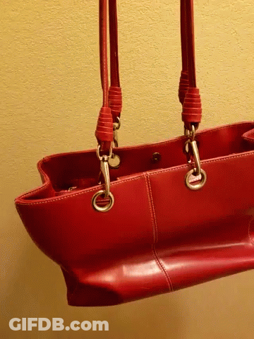 A Red Purse Is Hanging On A Yellow Wall With Two Handles GIF