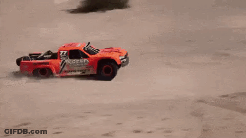 A Red Rc Truck Is Flying Through The Air On A Dirt Road . GIF
