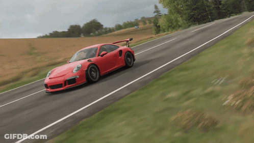 A Red Sports Car Is Driving Down A Road With Grass On The Side GIF