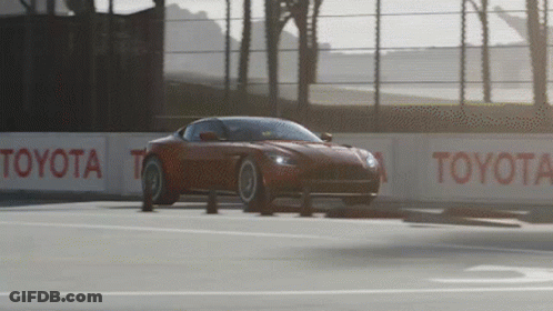 A Red Sports Car Is Driving On A Race Track With Toyota Signs Along The Side GIF