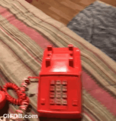 A Red Telephone Is Sitting On A Bed With A Red Cord GIF