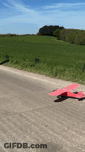A Red Toy Airplane Is Sitting On The Side Of A Road GIF
