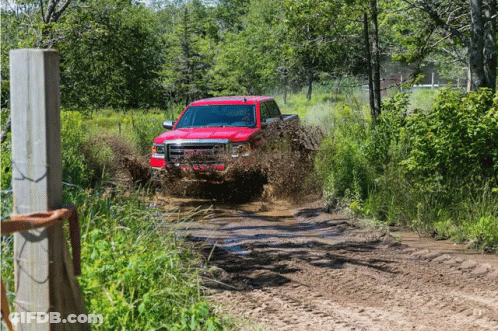 A Red Truck Drives Through A Muddy Field GIF
