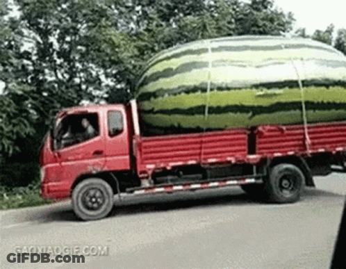 A Red Truck Is Carrying A Large Watermelon On The Back Of It . GIF