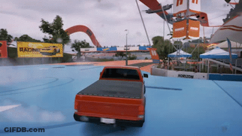 A Red Truck Is Driving On A Blue Track With A Horizon Sign In The Background GIF