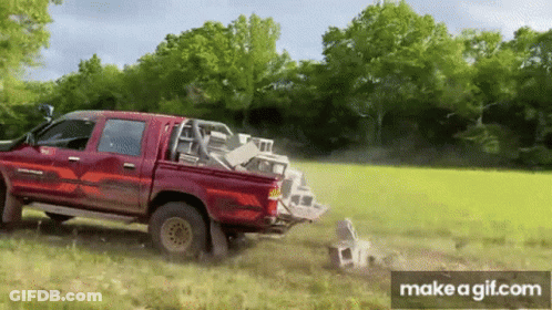 A Red Truck Is Driving Through A Grassy Field With A Pile Of Bricks In The Back . GIF