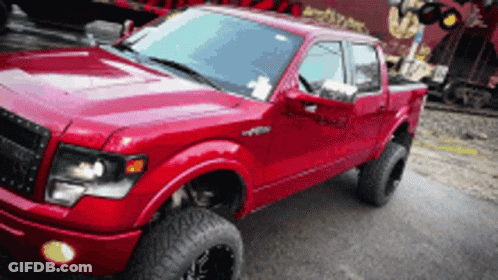 A Red Truck Is Parked On The Side Of The Road In Front Of A Train GIF